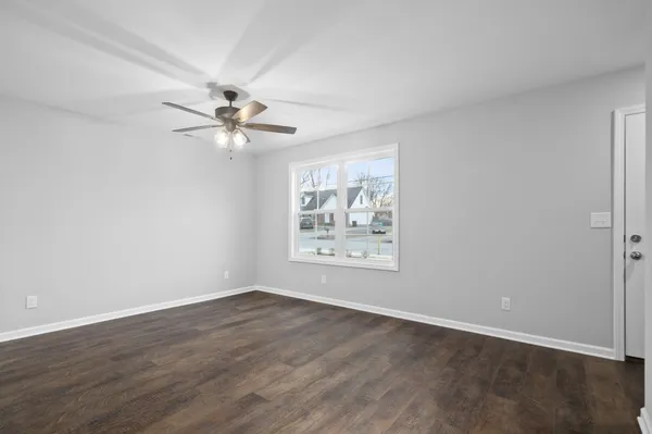 an empty room with wooden floor chandelier fan and windows