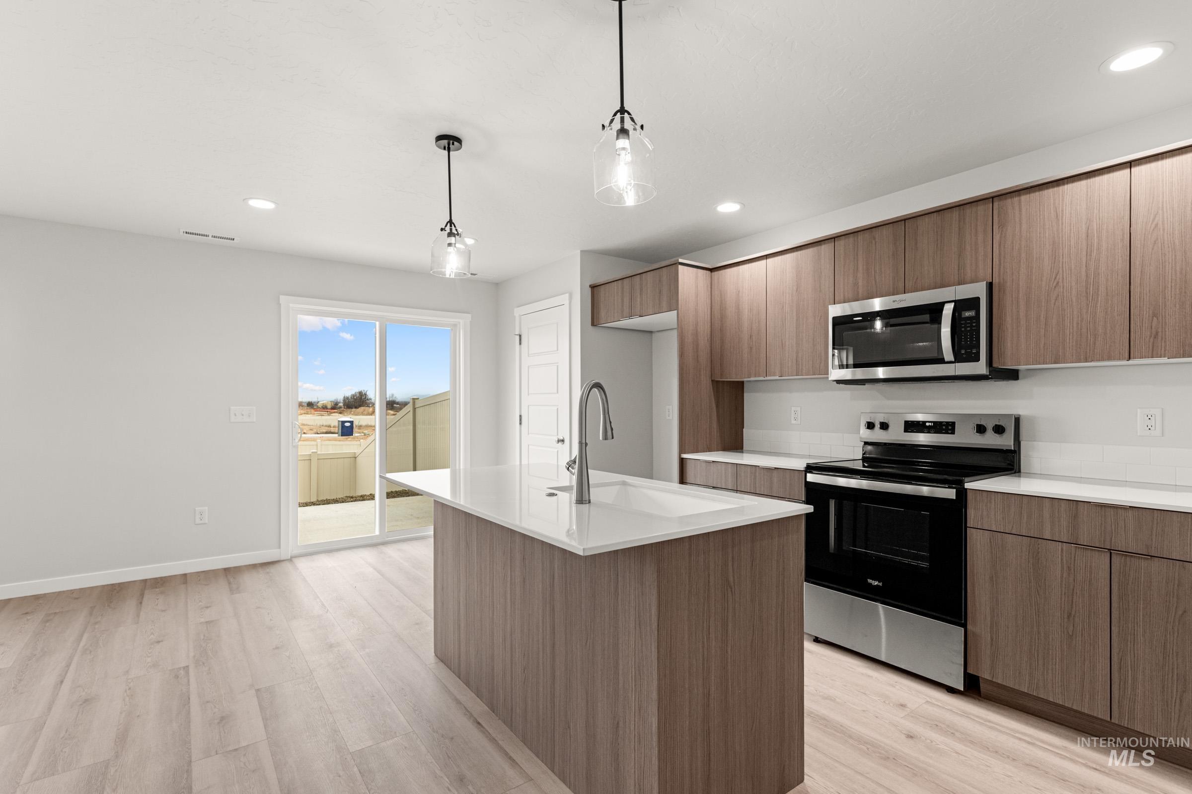 10824 Rutland Street Caldwell, ID 83605 - Photo 6 of 20 Kitchen with stainless steel appliances, modern cabinets, an island with sink, decorative light fixtures, and light wood-style flooring