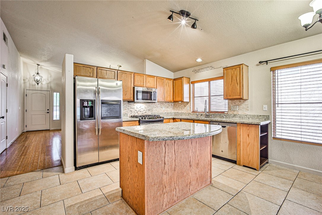 5128 Fall Meadows Avenue Las Vegas, NV 89130 - Photo 10 of 34 Kitchen featuring stainless steel appliances, vaulted ceiling, light stone counters, tasteful backsplash, and a center island
