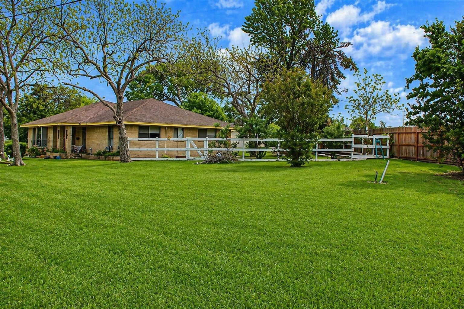 206 Riverside Street Highlands, TX 77562 - Photo 2 of 12 Expansive green backyard stretching well beyond the home, framed by mature trees and classic white rail fencing, a rare half acre canvas with endless potential.