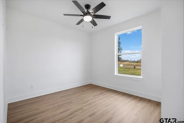 an empty room with wooden floor chandelier fan and windows