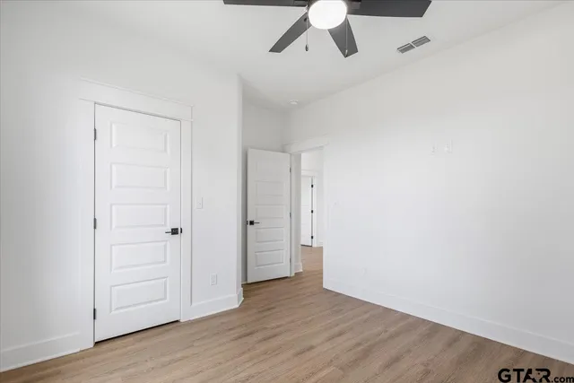 an empty room with wooden floor fan and windows