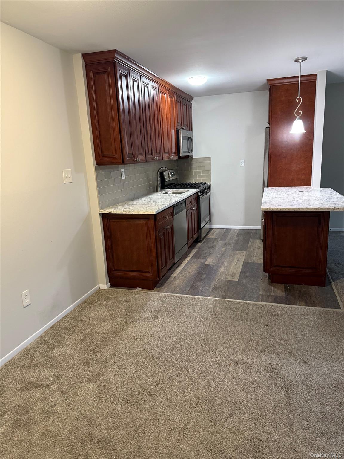 460 Old Town Road, Unit 8L Port Jefferson Station, NY 11776 - Photo 2 of 7 Kitchen featuring hanging light fixtures, light stone countertops, stainless steel appliances, tasteful backsplash, and dark carpet