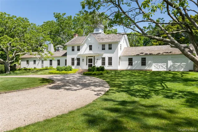 a view of a white house with a big yard plants and large trees