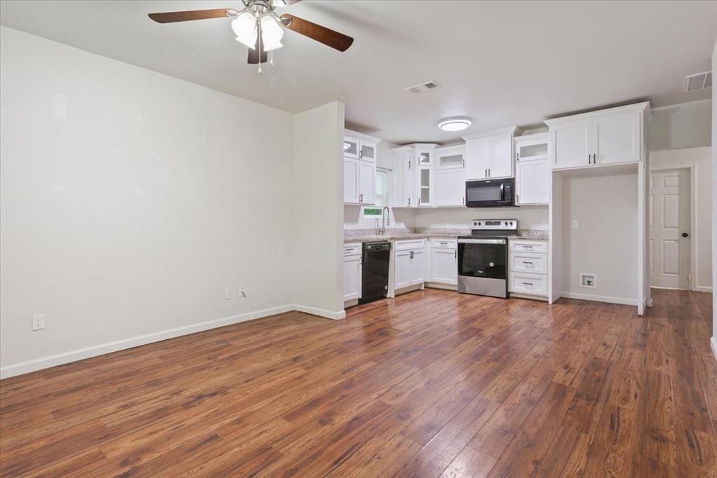 3109 North 20th Street Waco, TX 76708 - Photo 7 of 24 Open-concept kitchen and living area featuring wood-finish flooring, white cabinetry, stainless steel appliances, and a ceiling fan with integrated lighting