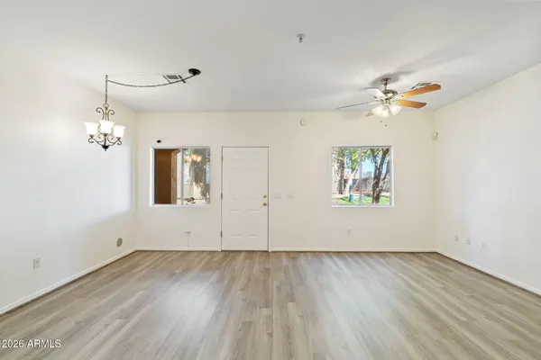 an empty room with wooden floor chandelier fan and windows