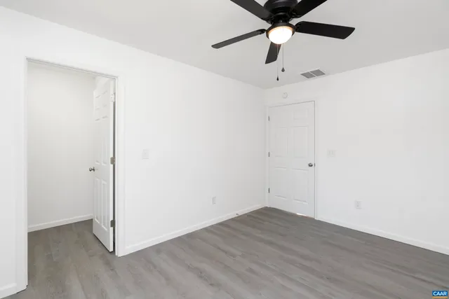 an empty room with wooden floor ceiling fan and windows