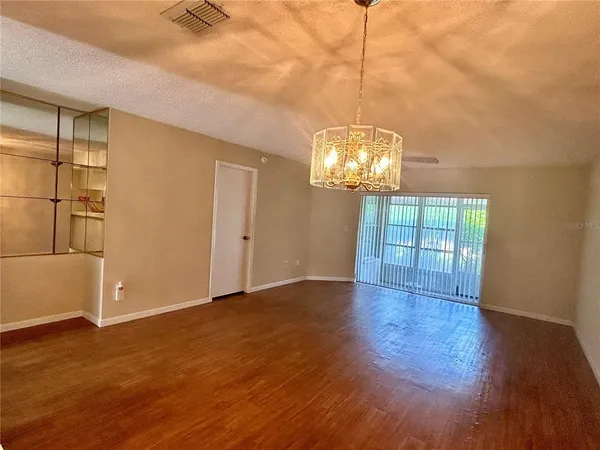 an empty room with wooden floor chandelier and windows