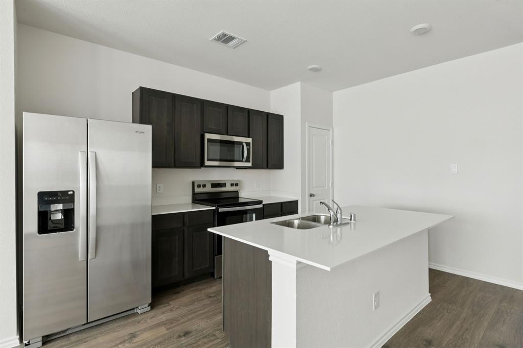 317 Clematis Street Princeton, TX 75407 - Photo 12 of 38 Kitchen featuring stainless steel appliances, a center island with sink, dark wood-style floors, and light stone countertops