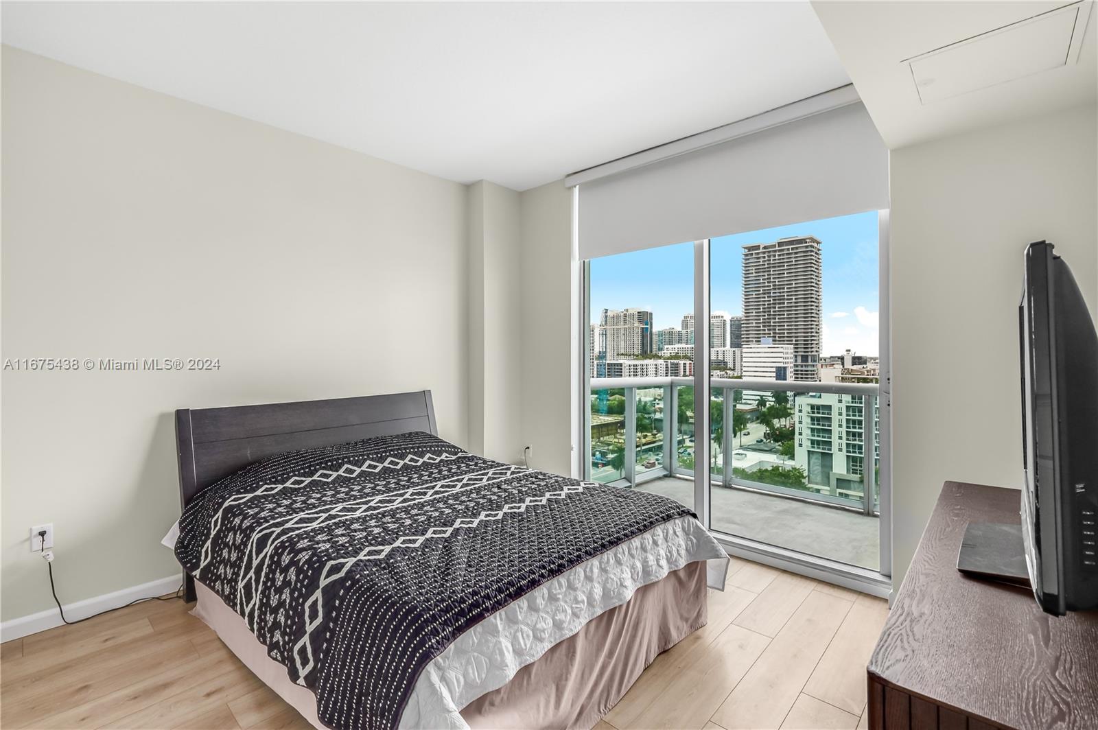 333 Northeast 24th Street, Unit 1206 Miami, FL 33137 - Photo 11 of 26 a bedroom with a large bed and a flat tv screen next to a window