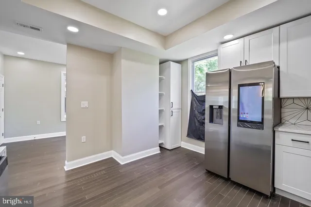 an empty room with wooden floor and a refrigerator