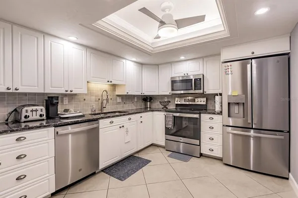 a kitchen with granite countertop a refrigerator stove and white cabinets