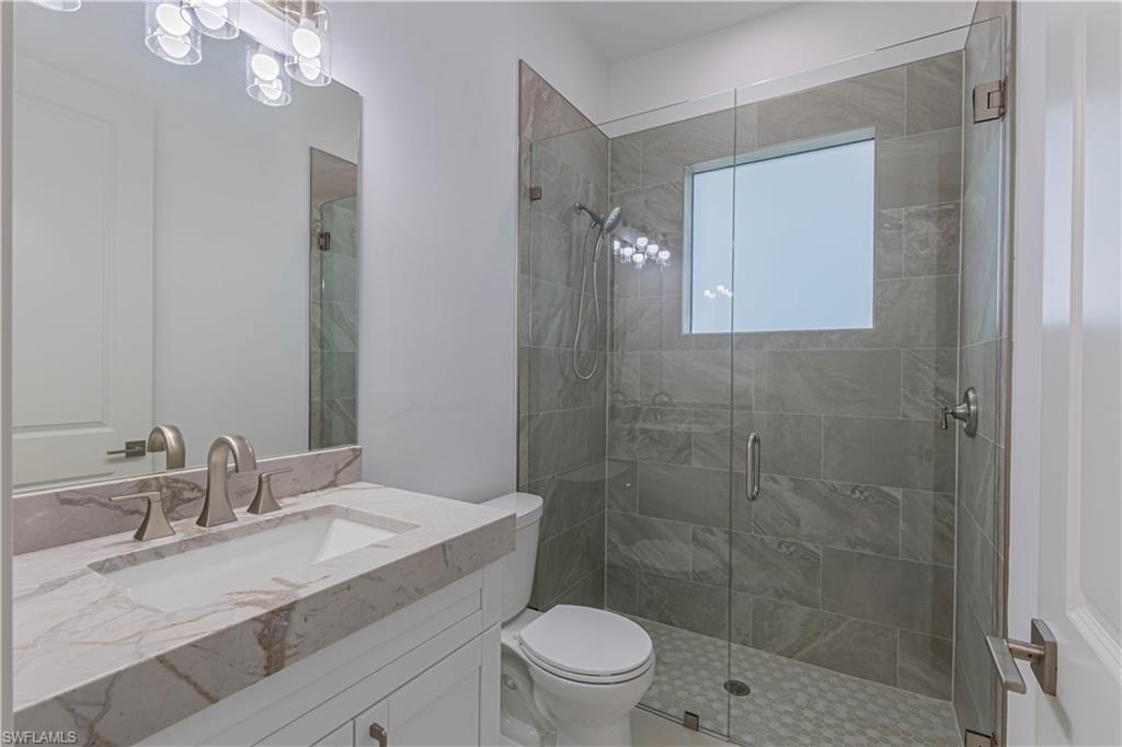 3074 Pine Tree Drive Naples, FL 34112 - Photo 12 of 18 a bathroom with a granite countertop sink toilet a mirror and shower