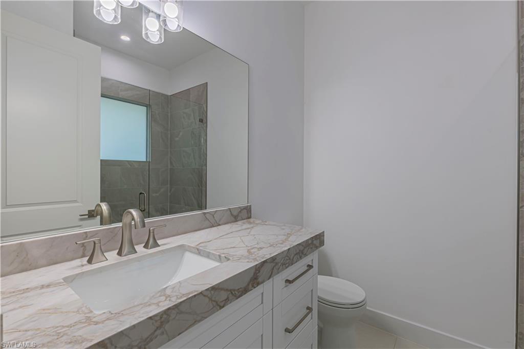 3074 Pine Tree Drive Naples, FL 34112 - Photo 13 of 18 a bathroom with a granite countertop sink a toilet and a mirror