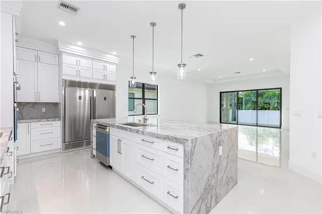 a kitchen with stainless steel appliances kitchen island granite countertop a stove a sink and a refrigerator with white cabinets