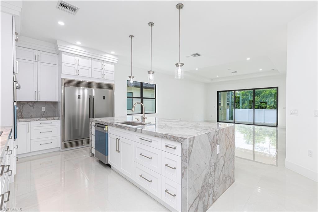 3074 Pine Tree Drive Naples, FL 34112 - Photo 4 of 18 a kitchen with stainless steel appliances kitchen island granite countertop a stove a sink and a refrigerator with white cabinets