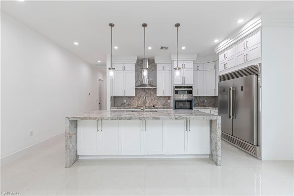 3074 Pine Tree Drive Naples, FL 34112 - Photo 7 of 18 a large kitchen with granite countertop a white stove top oven a refrigerator and white cabinets
