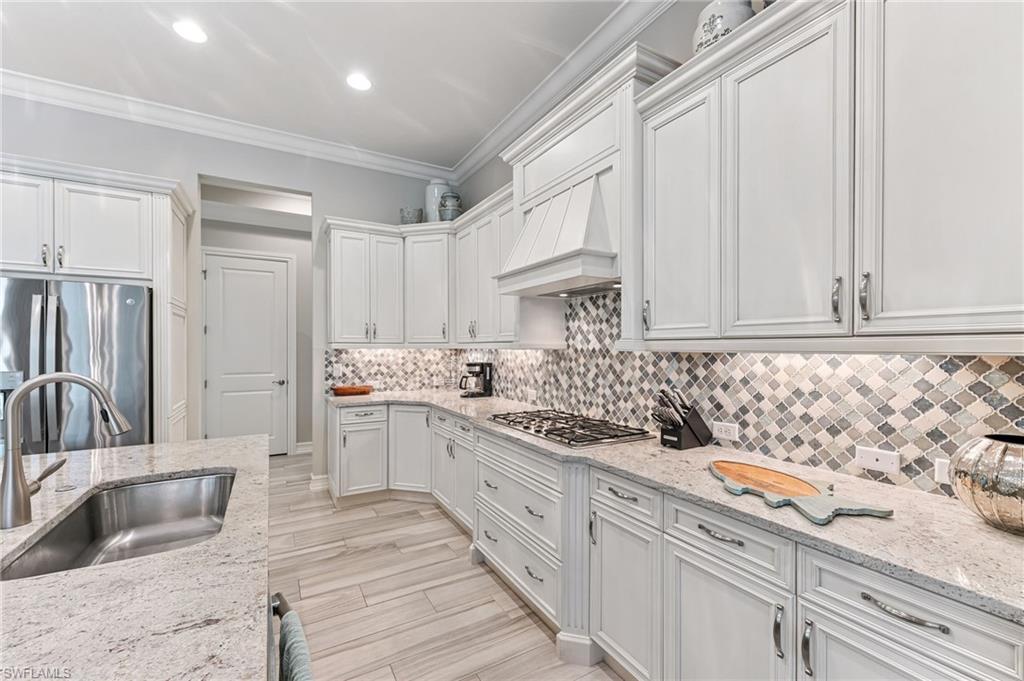 11974 Maidstone Court Naples, FL 34120 - Photo 14 of 45 Kitchen with appliances with stainless steel finishes, ornamental molding, white cabinetry, backsplash, and custom exhaust hood