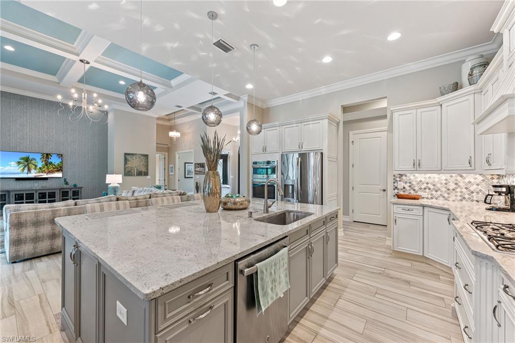 11974 Maidstone Court Naples, FL 34120 - Photo 45 of 45 Kitchen featuring stainless steel appliances, a center island with sink, crown molding, open floor plan, and light stone counters