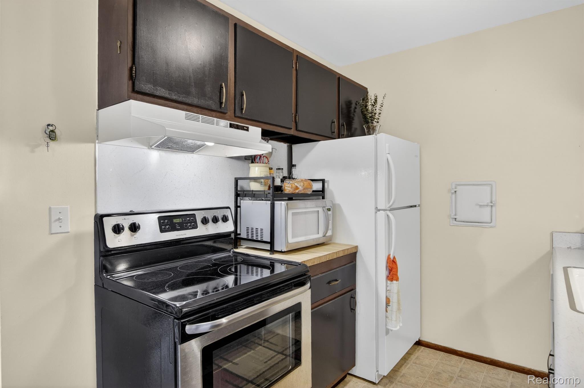 24111 Meridian Road, Unit 116 Grosse Ile, MI 48138 - Photo 13 of 26 Kitchen featuring dark wood cabinetry, white appliances, and a built-in range hood