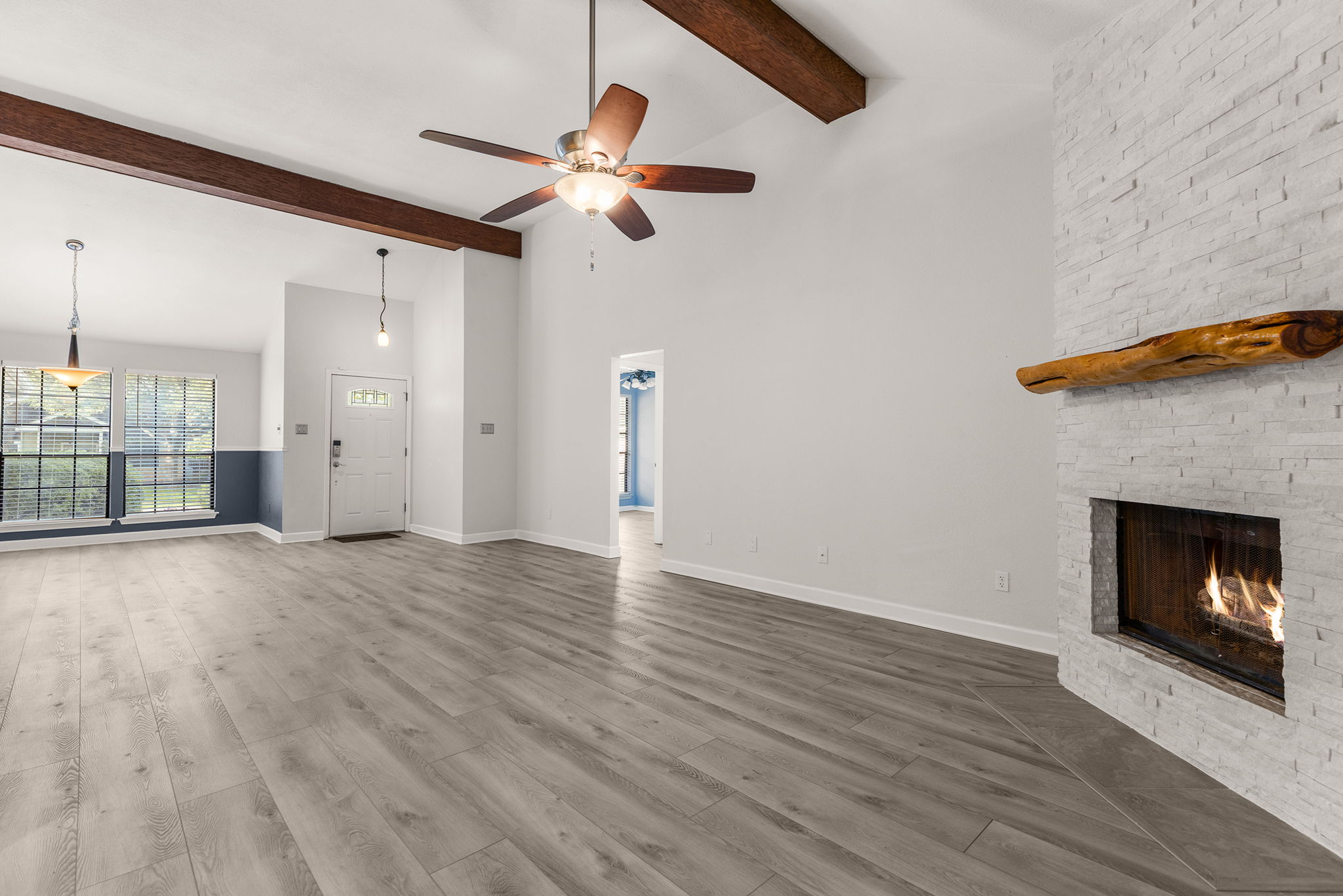 2409 Water Well Lane Austin, TX 78728 - Photo 7 of 22 Spacious living area featuring light wood-finish flooring, a white stacked stone fireplace with a live edge wood mantle, vaulted ceilings with exposed wood beams, and an entry door with frosted glass inserts