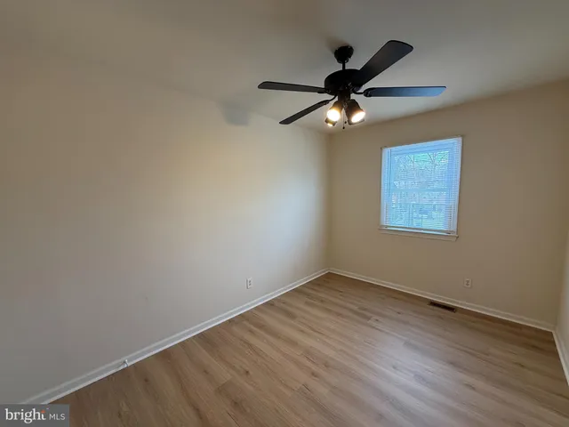 an empty room with wooden floor ceiling fan and window