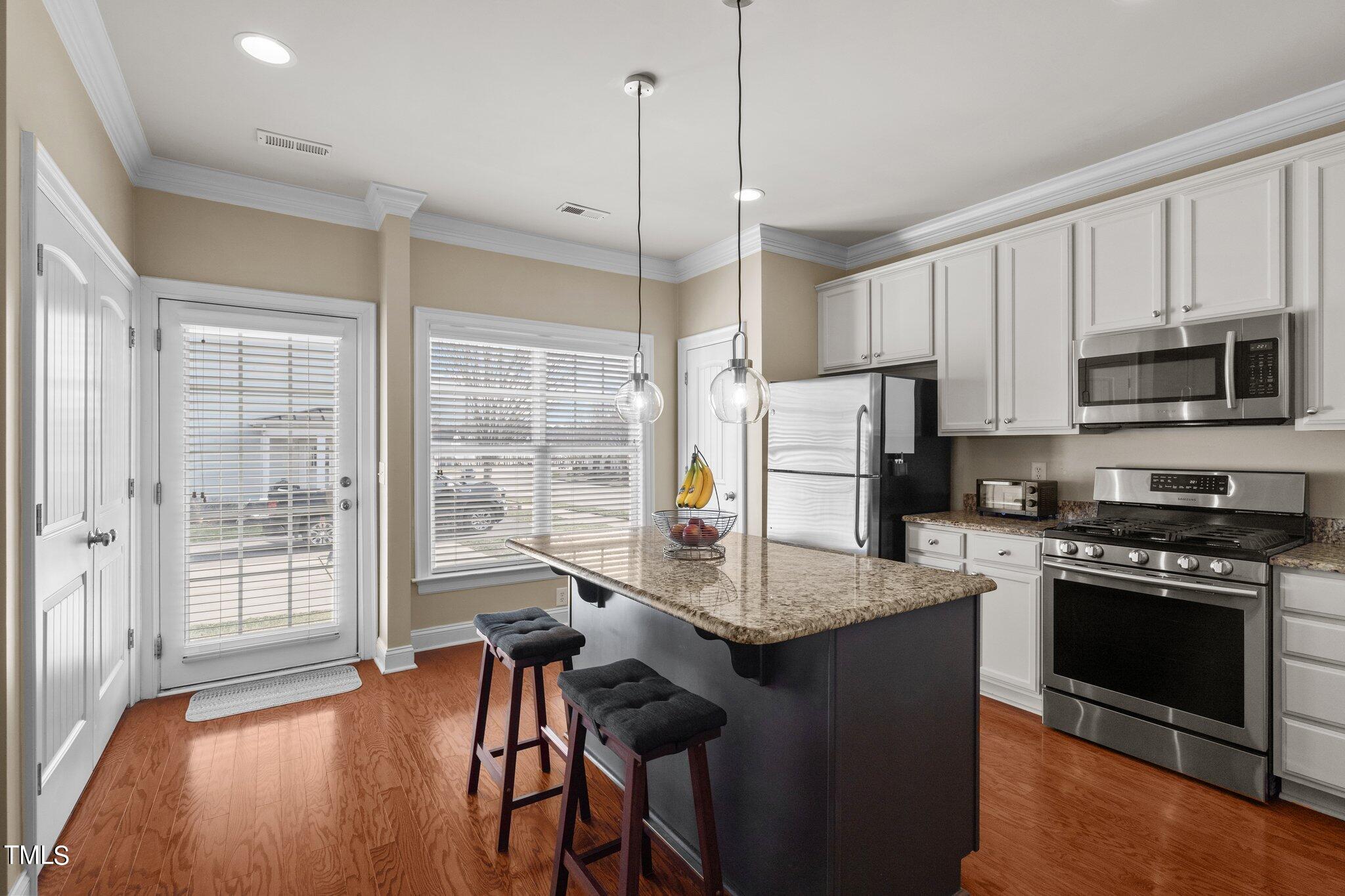 7765 Courtney Estates Drive Raleigh, NC 27617 - Photo 11 of 37 a kitchen with kitchen island a stove a sink and a refrigerator with wooden floor