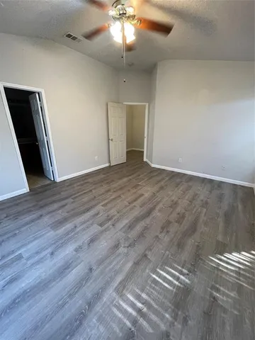 a view of an empty room with wooden floor and a ceiling fan