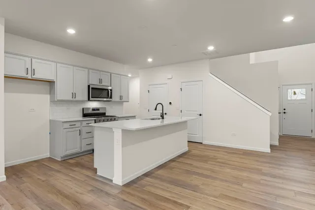 a large white kitchen with wooden floor and stainless steel appliances