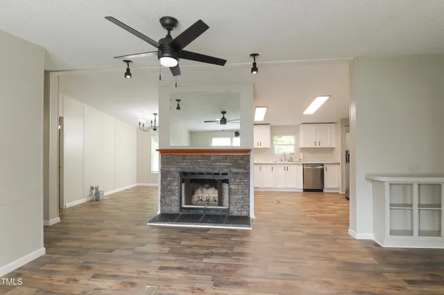 an empty room with wooden floor a fireplace and a kitchen view