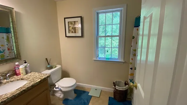 a bathroom with a granite countertop toilet a sink and a window