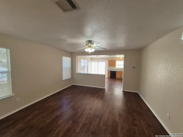 an empty room with wooden floor chandelier and windows