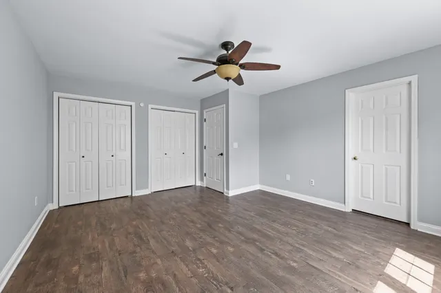 an empty room with wooden floor ceiling fan and windows
