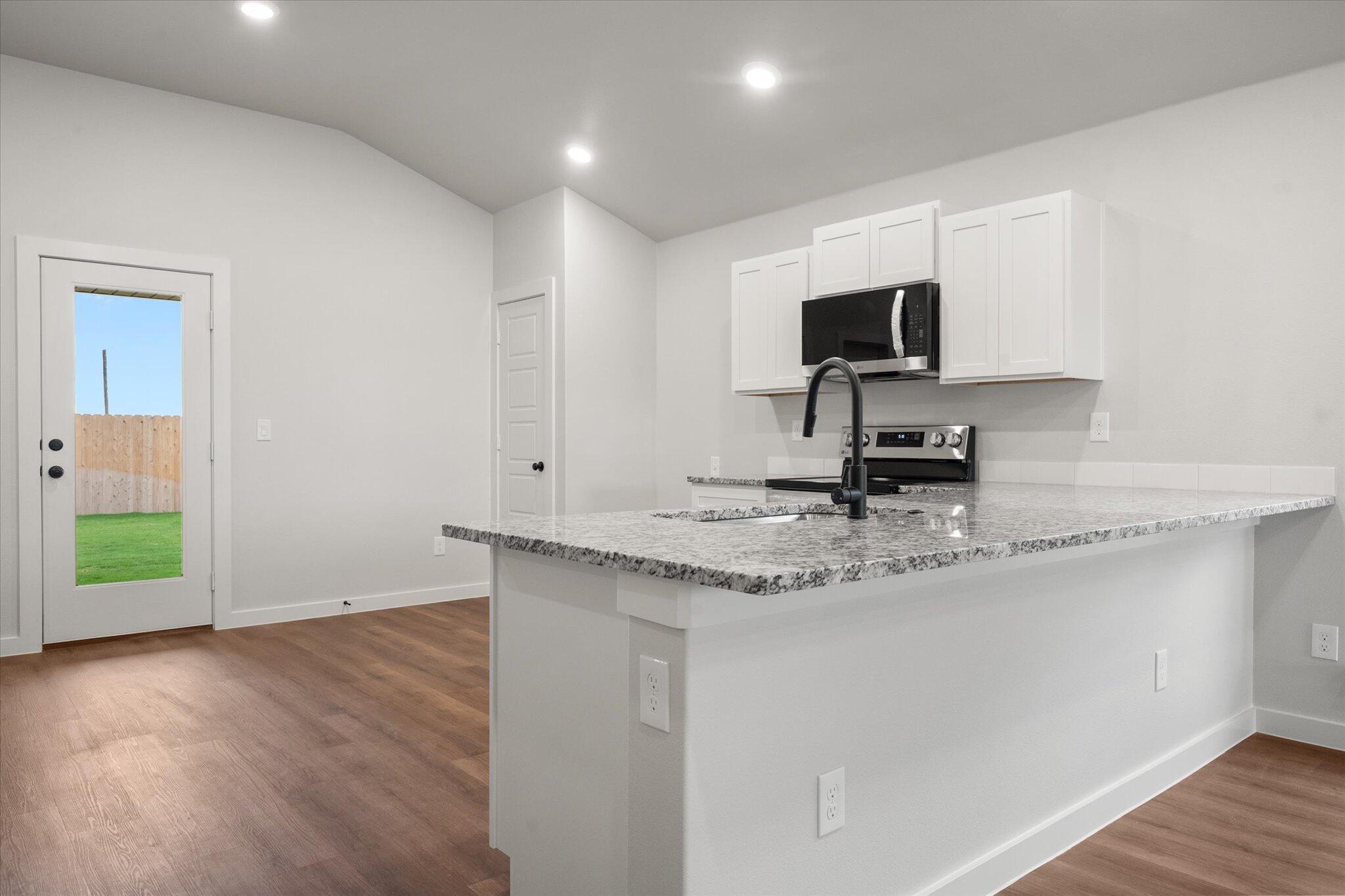 8607 29th Street Lubbock, TX 79407 - Photo 8 of 20 a kitchen with stainless steel appliances granite countertop a sink a stove and a microwave oven with wooden floor