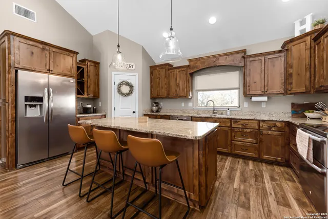 a kitchen with stainless steel appliances granite countertop a kitchen island a stove a refrigerator a sink a dining table and chairs with wooden floor