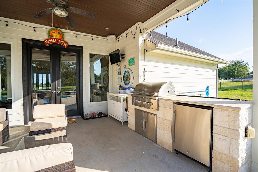 1920 Meander Road Granbury, TX 76049 - Photo 26 of 40 Covered outdoor patio featuring a built-in stone outdoor kitchen with a stainless steel grill and refrigerator, a dark wood-paneled ceiling, and a ceiling fan