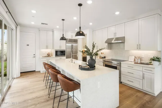 a kitchen with stainless steel appliances kitchen island a table chairs sink and cabinets