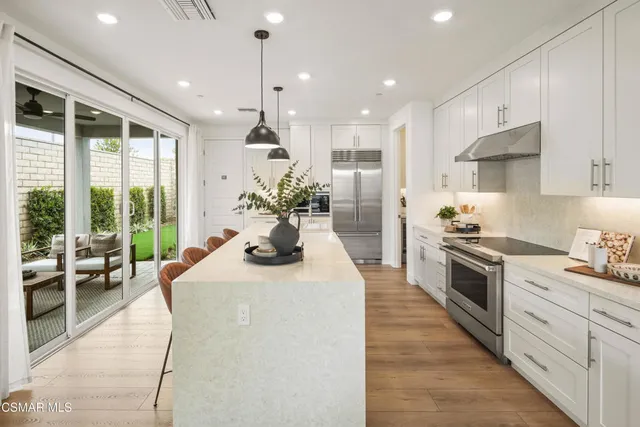 a kitchen with stainless steel appliances kitchen island granite countertop a stove a sink a refrigerator and white cabinets with wooden floor