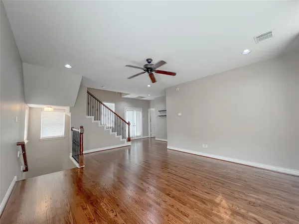 a view of an empty room with wooden floor and a ceiling fan