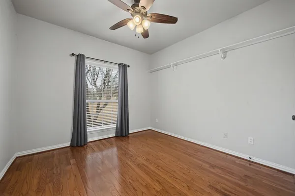 an empty room with wooden floor chandelier fan and windows