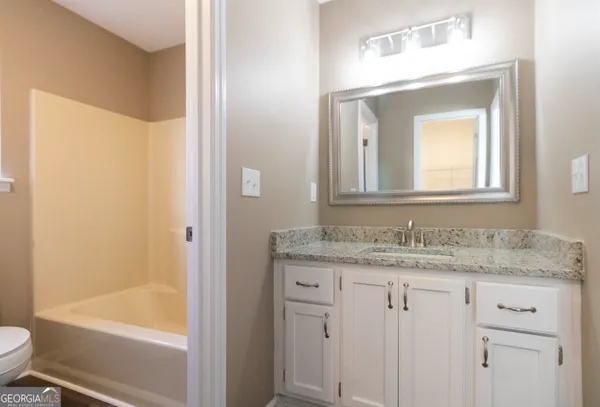 a bathroom with a granite countertop sink vanity mirror bathtub and toilet
