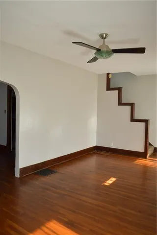 a view of an empty room with wooden floor and a ceiling fan