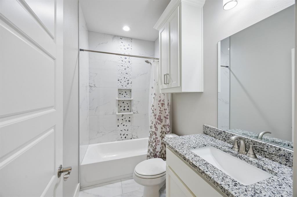 612 Frisco Road Sherman, TX 75090 - Photo 6 of 25 Full bathroom with a white tub and shower combination, featuring a tiled surround with a decorative pebble-style accent