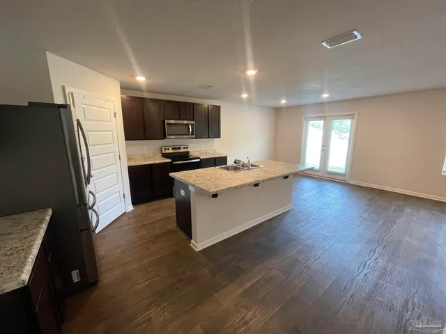 a kitchen with stainless steel appliances granite countertop a refrigerator a sink dishwasher a stove and white countertops with wooden floor