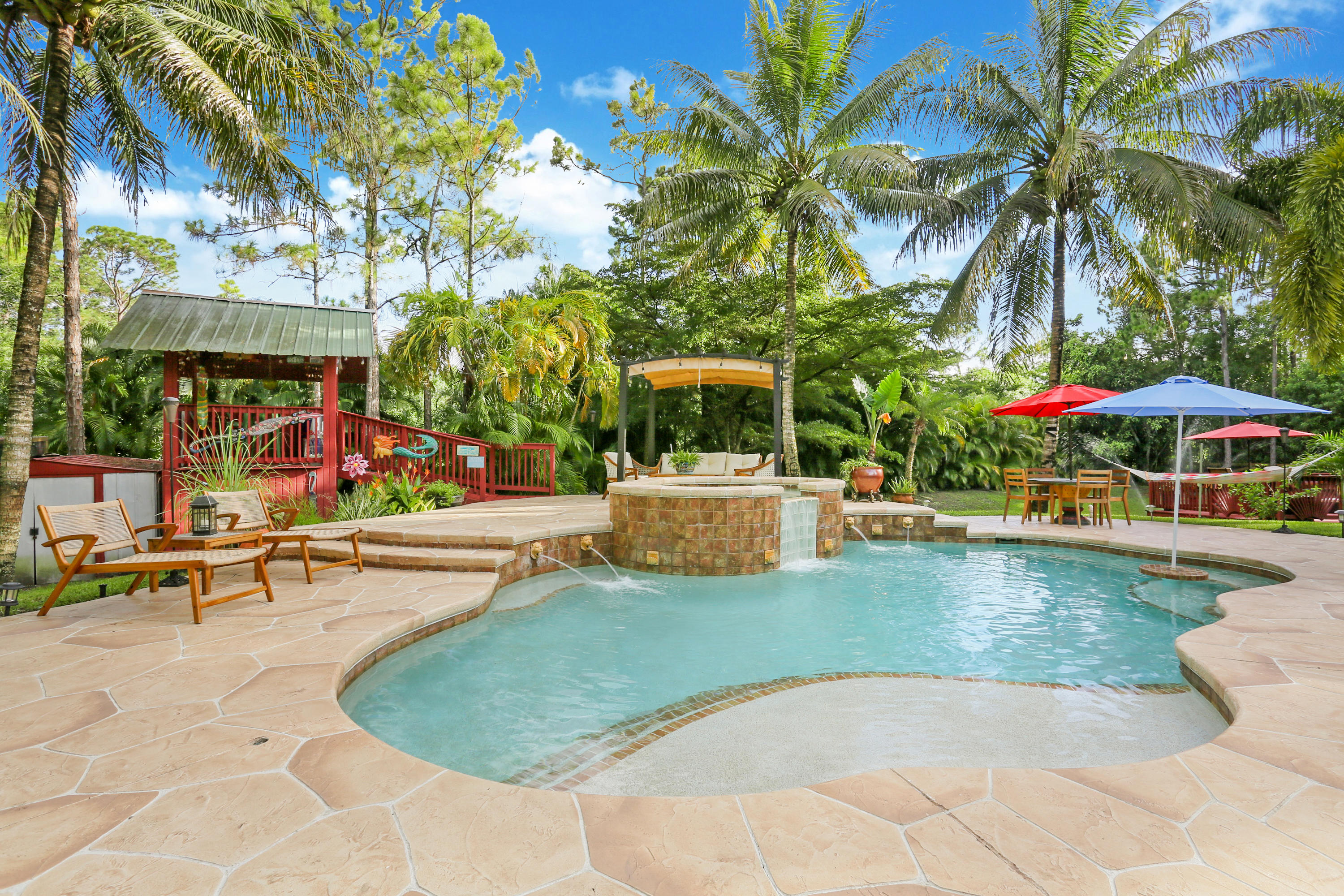 18604 43rd Road North Loxahatchee, FL 33470 - Photo 12 of 40 a view of a swimming pool with a table and chairs under palm trees