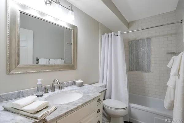 a bathroom with a granite countertop sink a toilet a mirror a vanity and shower