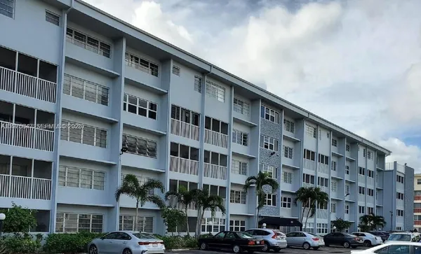 a front view of a building with lot of cars and trees