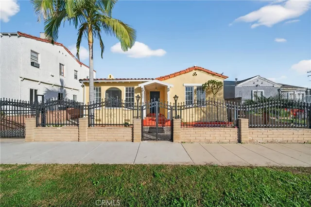 a view of a white house in front of a yard with plants and palm trees