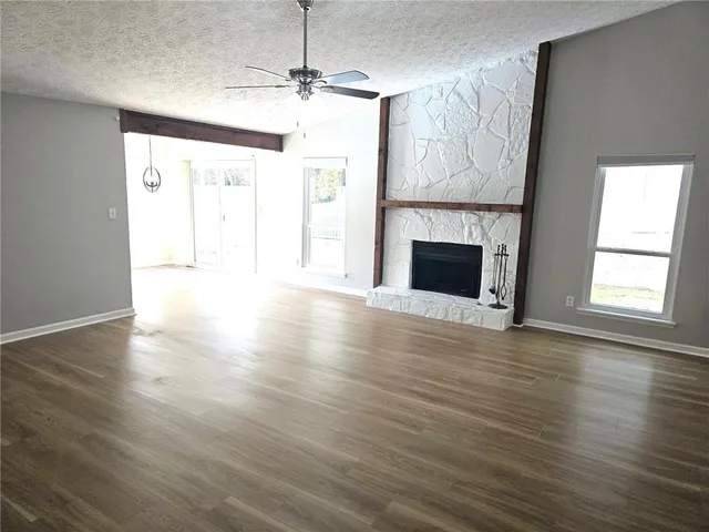 a view of an empty room with wooden floor fireplace and a window