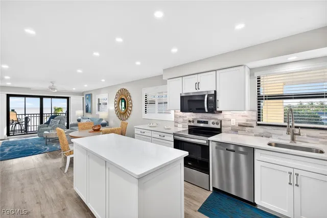 a large white kitchen with granite countertop a stove a sink a dining table and chairs with wooden floor